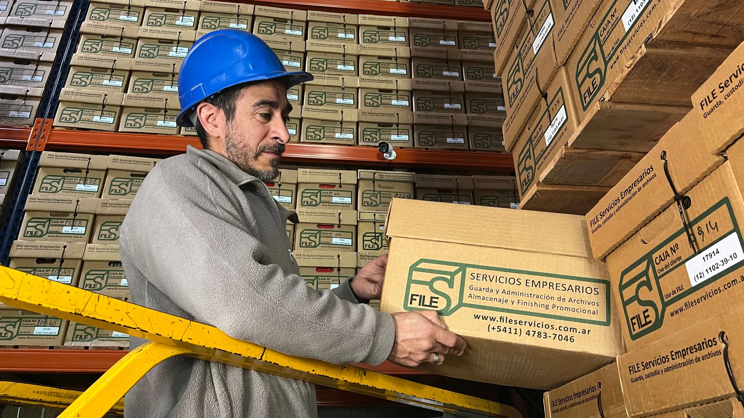 Empleado de FILE con casco azul manipulando una caja en las estanterías del depósito